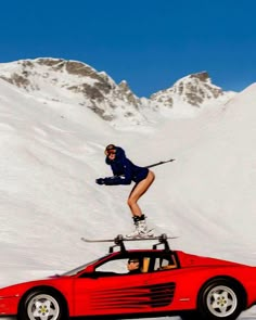 a person on skis jumping over a red sports car in the middle of snow