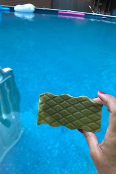 a hand holding a sponge next to a swimming pool