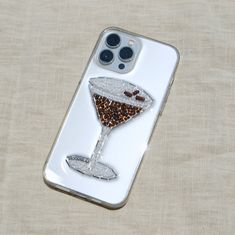 a phone case with a martini glass on it sitting on top of a beige cloth