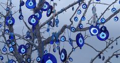 a tree with blue evil eye ornaments hanging from it's branches in front of a cloudy sky