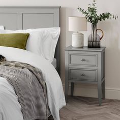 a bed with white sheets and pillows next to a night stand on a wooden floor