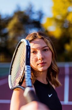 a woman holding a tennis racquet on top of a tennis court with trees in the background