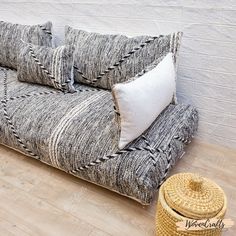 a couch that has some pillows on it and a basket next to it with a pillow in front of it