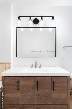 a bathroom vanity with two sinks and three lights on the mirror above it is an empty toilet