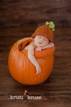 a baby in a pumpkin wearing a knitted hat and sleeping on it's side