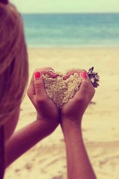 a woman holding sand in her hands with a quote about love on the beach behind her