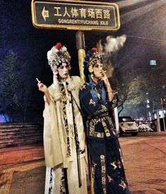 two people dressed in costumes standing next to a street sign