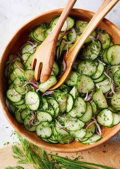 a wooden bowl filled with cucumbers and onions next to two wooden spoons