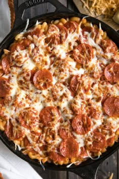 a pepperoni pizza in a cast iron skillet on a wooden table with cheese