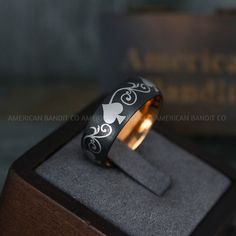 a ring with an intricate design on it sits in a wooden box next to a book