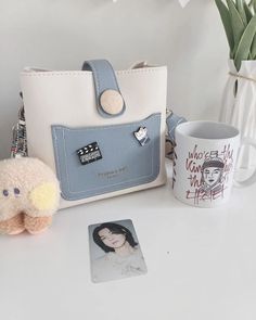 a white purse sitting on top of a table next to a coffee cup and small stuffed animal