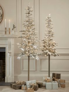 two christmas trees with presents under them in front of a fireplace