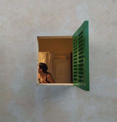 a woman is looking out the window of a house with green shutters on it