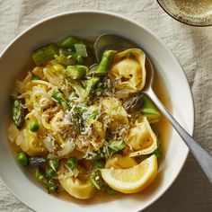 a white bowl filled with pasta and asparagus next to a glass of wine