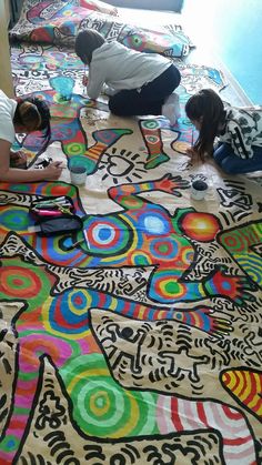 three people are laying on the floor with colorful designs painted on it and one person is painting