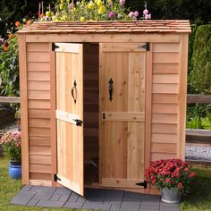 a wooden storage shed with its doors open and flowers growing on the top shelf above it