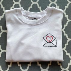 a white t - shirt with a heart in an envelope embroidered on it