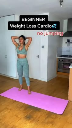 a woman standing on a pink yoga mat with her arms behind her head