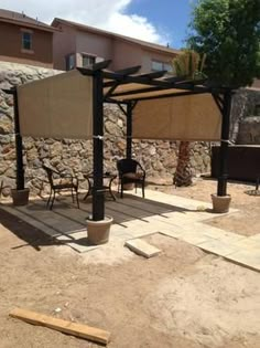 an outdoor patio with several chairs and tables under a shade structure in the middle of a yard