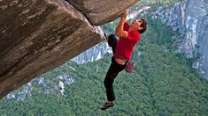 a man standing on the edge of a cliff with his hands in the air while climbing