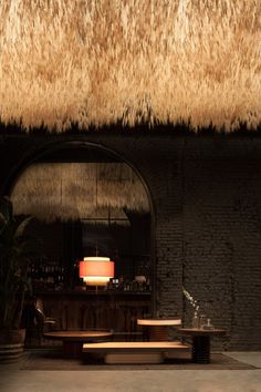 the interior of a restaurant with tables and stools in front of a thatched roof