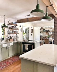 Achieve your kitchen goals with these soft green kitchen shaker cabinets topped with white and gray marble countertops. Stained wood and black metal shelves are mounted to a white subway tile backsplash above the counter. Complement the color of the cabinets with green metal pendant light fixtures...   Image: littlefarmbigcity