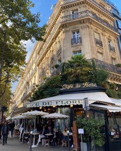 people sitting at tables in front of a tall building with plants growing on the roof