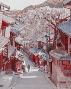 a man walking down a street next to tall red buildings with trees in the background