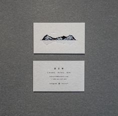 two white business cards with mountains in the background on a gray surface, one has a black and white logo