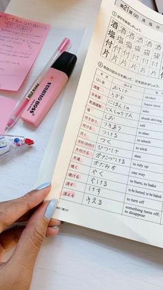 a person is holding a pen and writing on a paper with japanese characters in it