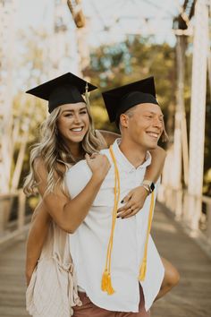 a man and woman in graduation gowns posing for a photo on a bridge with their arms around each other