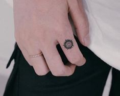 a person's hand with a small sun tattoo on their left ring and the other half of her finger