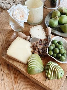 a wooden cutting board topped with different types of cheese and fruit on top of a table