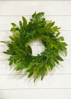 a green wreath hanging on the side of a white wooden wall next to a potted plant