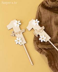 two paper cutouts with name and flowers on them sitting next to a brown blanket