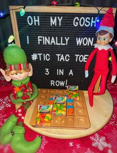 two elfs are sitting in front of a sign that says oh my gosh i finally won tic tac toe 3 in a row