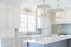 a kitchen with white cabinets and an island in the middle is lit by pendant lights