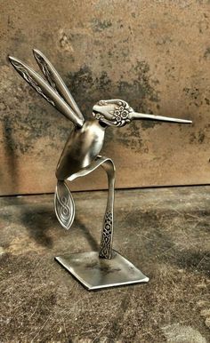 a metal bird sculpture sitting on top of a piece of wood next to a wall