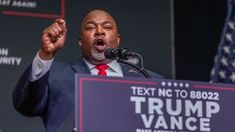 a man speaking at a podium with an american flag in the background