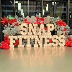 the words snap fitness are lit up in front of balloons and streamers with lights