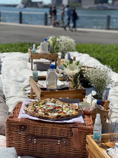 an outdoor picnic with pizza and drinks on the grass next to the water in front of some people