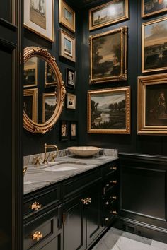 a bathroom with black walls and gold framed pictures on the wall above the sink, along with a marble countertop