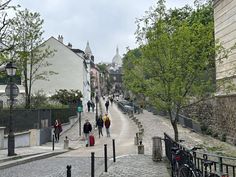 several people walking down a cobblestone street with bicycles parked on the side walk