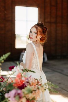 a woman with red hair wearing a white dress standing in front of a flower arrangement