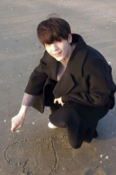 a young boy is writing in the sand at the beach with his hand and heart drawn in the sand