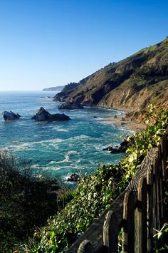 an ocean view from the top of a hill with a wooden fence in front of it