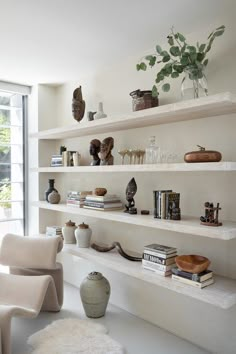 a living room filled with lots of white furniture and shelves covered in vases on top of them