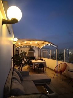 an outdoor living area with couches, tables and lights on the side of it