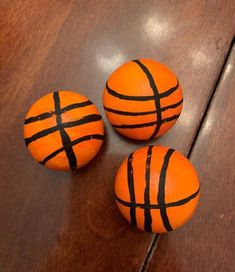 three orange basketballs sitting on top of a wooden table with black lines painted on them