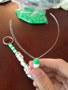 a person holding a green and white beaded keychain on top of a wooden table